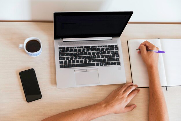 Foto spazio di lavoro con computer con schermo nero mani che prendono appunti su blocco appunti tazza di caffè e smartphone persone irriconoscibili spazio di copia