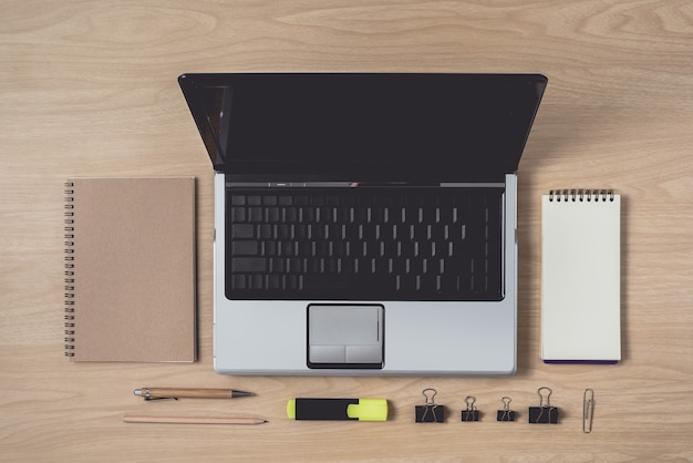 Photo workspace with diary or notebook and laptop, pen, pencil, hightlight pen, metal clip on wood