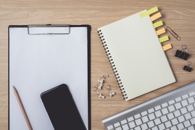 Workspace with diary or notebook and smart phone, clipboard, keyboard, pencil, sticky notes on wooden 