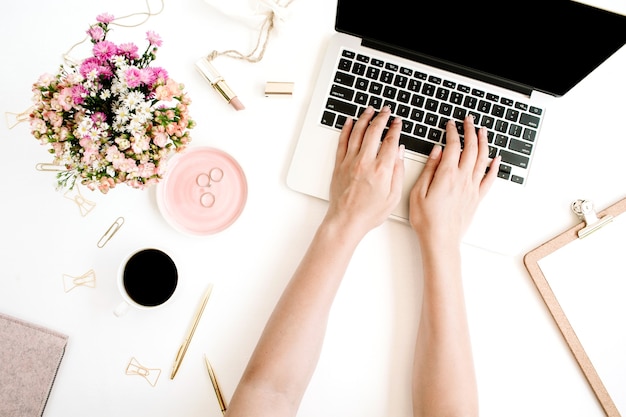 Area di lavoro con le mani della ragazza, laptop, bouquet di fiori di campo, tazza di caffè, penna dorata e clip, appunti