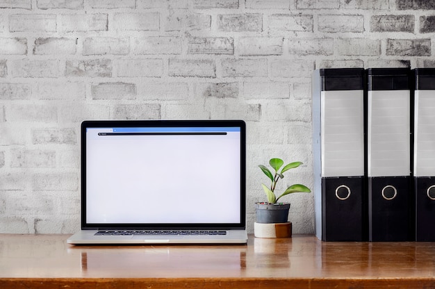 オフィスで木製のテーブルとレンガの壁にラップトップコンピューターとファイルフォルダーを持つワークスペース。