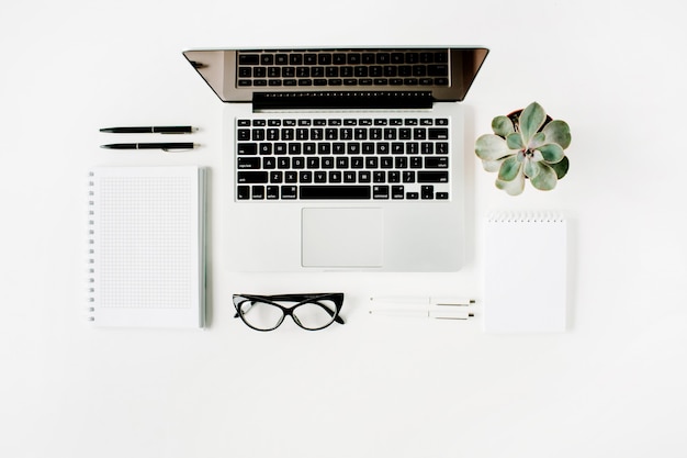 Area di lavoro con laptop, diario, succulente e bicchieri su bianco.