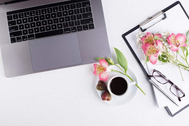 Foto area di lavoro con laptop, blocco note, tablet, occhiali, tazza di caffè nero e un fiore di giglio peruviano su uno sfondo bianco