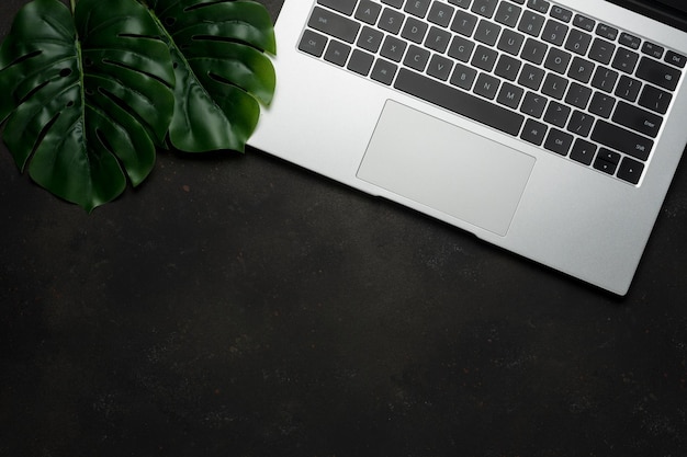 Workspace with laptop and palm leaves on black background Flat lay top view office table desk