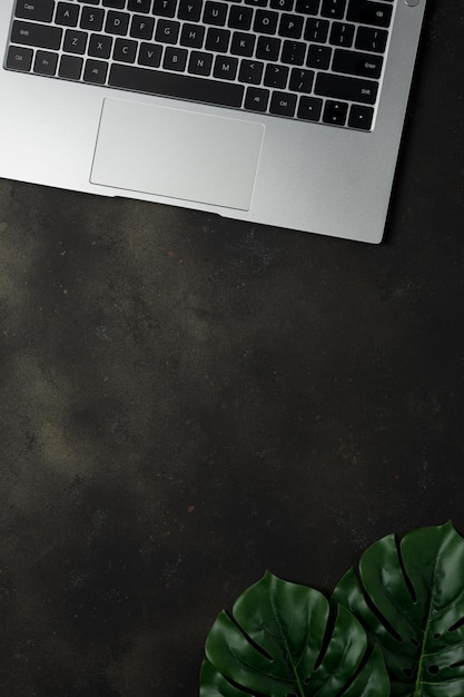 Workspace with laptop and palm leaves on black background Flat lay top view office table desk