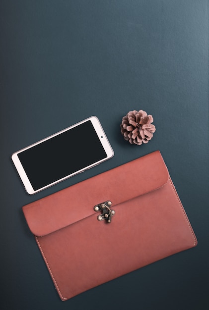 Workspace with mobile phone, leather bag and pine cone