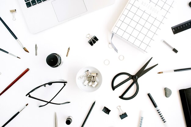 Workspace with notebook, laptop, scissors, glasses, pen on white.