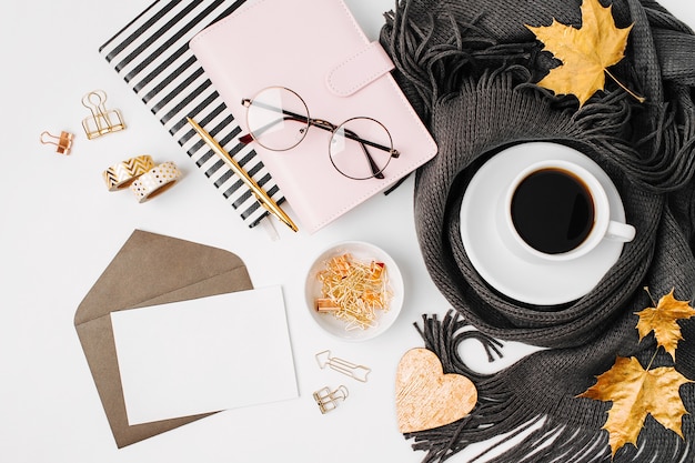 Workspace with notebook with empty card, coffee cup wrapped in scarf,  glasses. Stylish office desk. Autumn or Winter concept.  Flat lay, top view