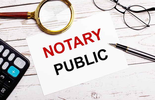 펜, 안경, 계산기, 돋보기 및 흰색 나무 테이블에 NOTARY PUBLIC의 텍스트가 있는 흰색 종이가 있는 작업 공간. 비즈니스 개념입니다.