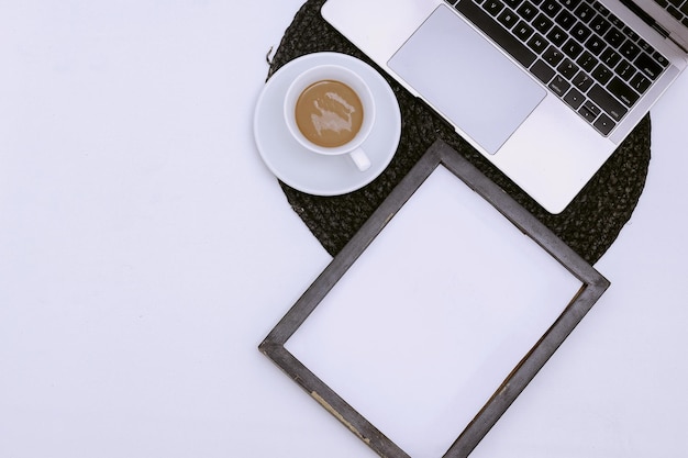 Area di lavoro con mockup di cornice per foto, tazza di caffè e laptop su sfondo bianco. compositi per l'home office