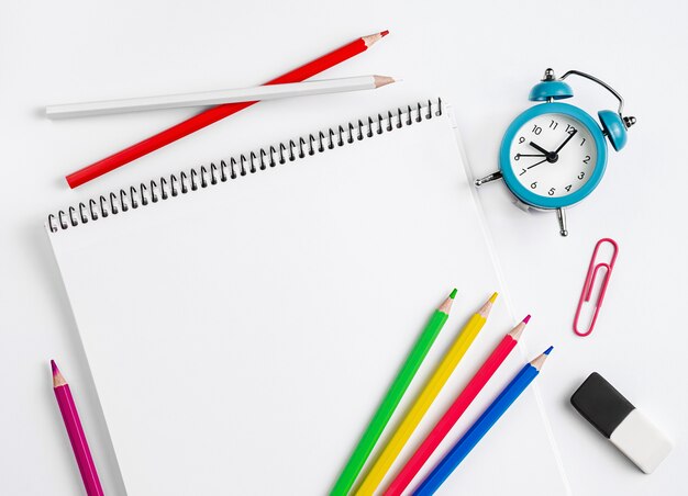 Workspace with school supplies, notebook, colorful pencils and clock. Flat lay, copy space.