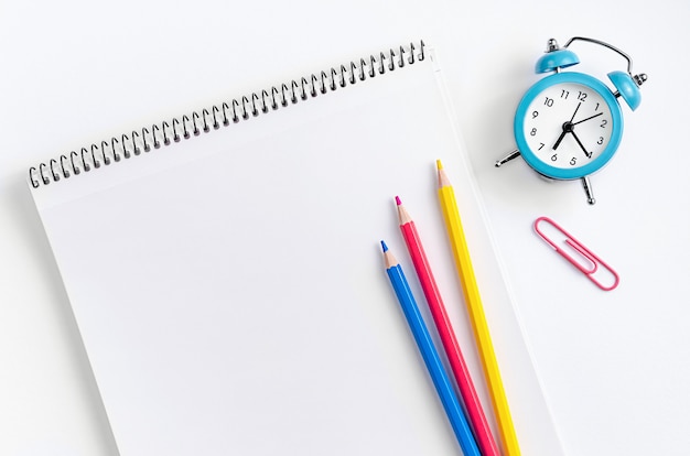 Workspace with school supplies, notebook, colorful pencils and clock. Flat lay..