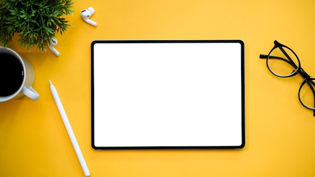 Workspace with tablet mockup eyeglasses stylus pen earbuds on yellow background top view