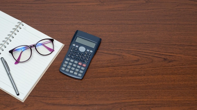 Workspace on wooden table top viewNotebook glasses calculator on table