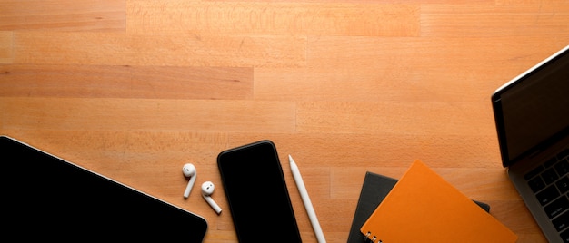 Worktable with copy space, laptop, smartphone, tablet and notebooks on wooden table