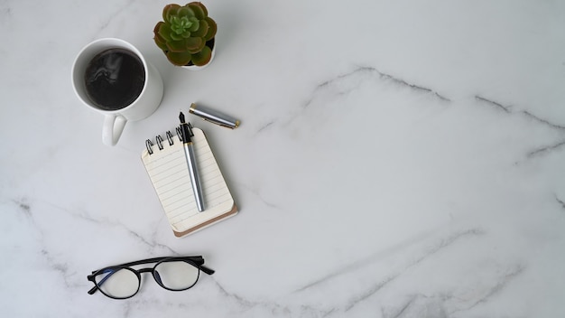 Worktable with notebook, coffee cup, cactus, glasses and copy space on marble surface