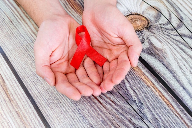 Красная лента Всемирного дня борьбы со СПИДом в руках на деревянном фоне