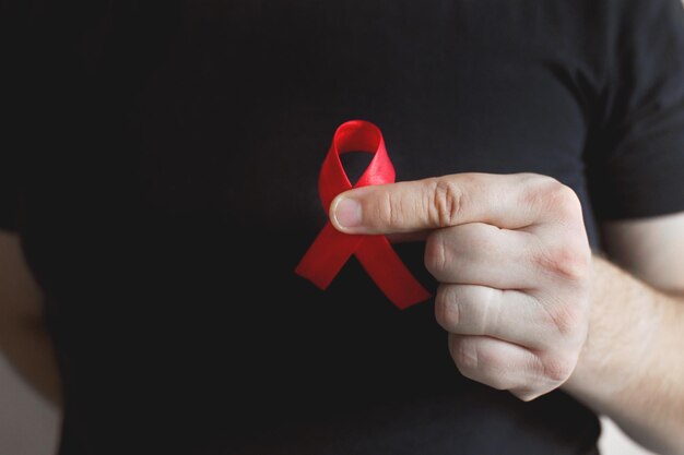 Giornata mondiale dell'aids e dell'hiv un uomo con una maglietta nera tiene un nastro rosso trasfusione e donazione di sangue