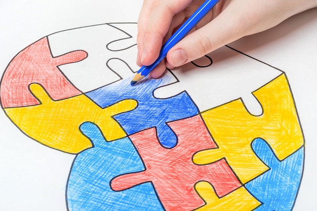 World Autism Awareness day. Children's hand draws heart from multi-colored puzzles. Mental health care concept.