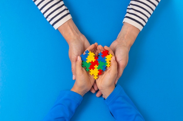 Foto concetto della giornata mondiale di consapevolezza sull'autismo mani di adulti e bambini che tengono un puzzle cuore su sfondo blu