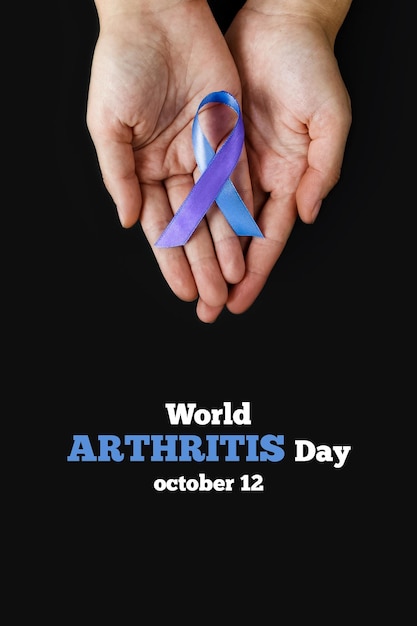 세계 자가면역 관절염의 날. 검정색 배경에 파란색 보라색 리본을 들고 있는 성인 손. RA 류마티스 관절염 질환. 세로로 사진.