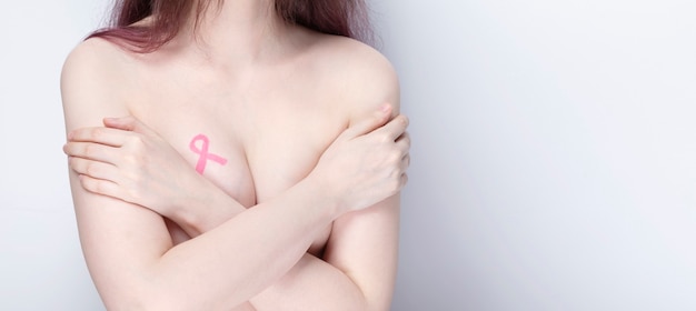 Photo world breast cancer day concept. woman covers her chest with her hands with painted pink ribbon. october breast cancer awareness month. copy space