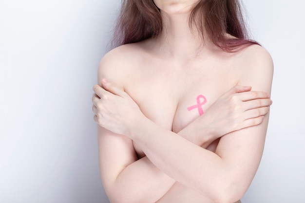 Foto concetto di giornata mondiale del cancro al seno. la donna si copre il petto con le mani con nastro rosa dipinto. ottobre mese della consapevolezza del cancro al seno.