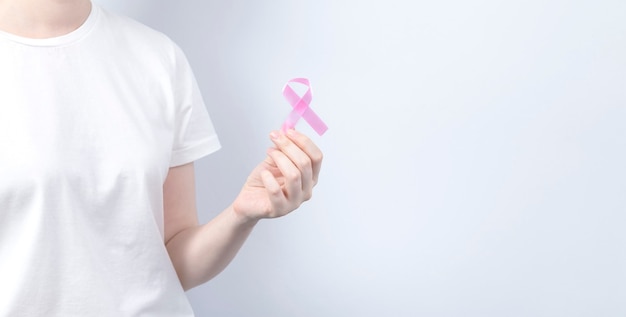 World Breast cancer day concept. Woman in white T-shirt holds pink ribbon in her hand. October Breast Cancer Awareness month. Copy space