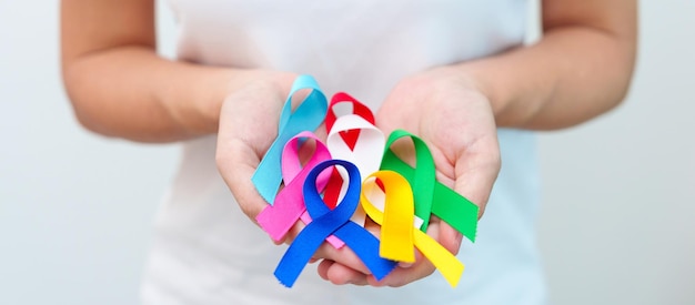 世界がんデー 2 月 4 日ブルー、レッド、グリーン、ホワイト、ピンク、ネイビー、ブルー、イエローのリボンを持っている手で、人々の生活や病気をサポートします。ヘルスケアと自閉症啓発デーのコンセプト。