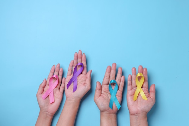 World cancer day. Hands of people holding colorful awareness ribbons for supporting people 