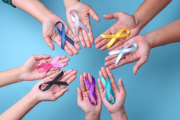 World cancer day. Hands of people holding colorful awareness ribbons for supporting people 