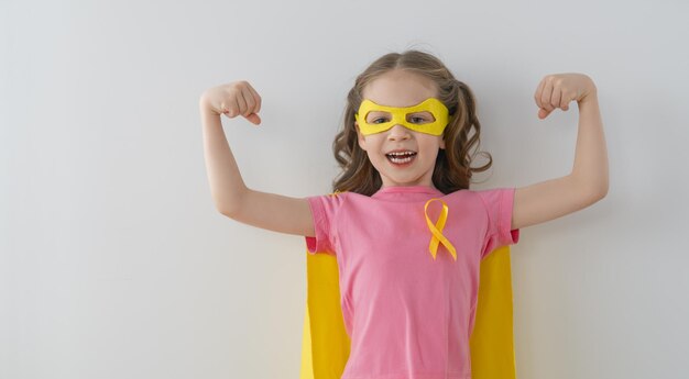 World Childhood cancer Day.  Girl in superhero costume with golden ribbon.