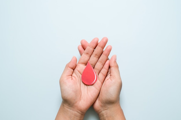 World diabetes day and blue ribbon awareness with red blood drop in woman hands isolated on a blue background. World diabetes day,14 november. Copy space. Top view