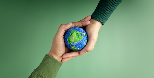 World Earth Day Concept Green Energy ESG Renewable and Sustainable Resources Environmental Care Hands of People Embracing a Handmade Globe Protecting Planet Together Top View