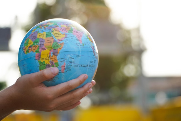 World environment day concept hand of a little girl holding the
world blurry green lawn background protect our world copy
space