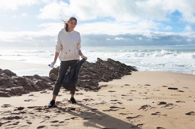 World environment day Female volunteer standing on beach with bag picking up garbage and cleaning the coastal zone