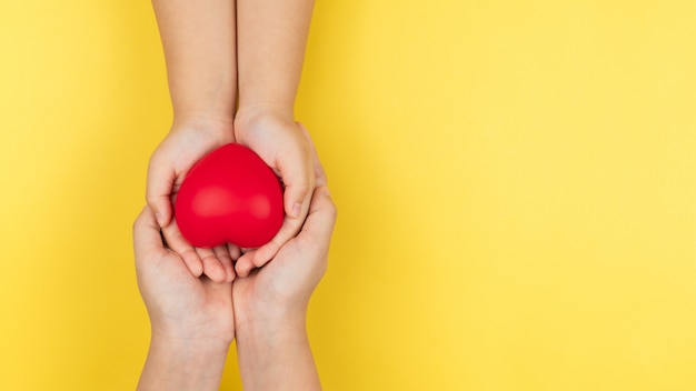 Mani della giornata mondiale della salute, dell'adulto e del bambino che tengono concetto rosso del cuore, di sanità, di amore e di assicurazione sulla famiglia