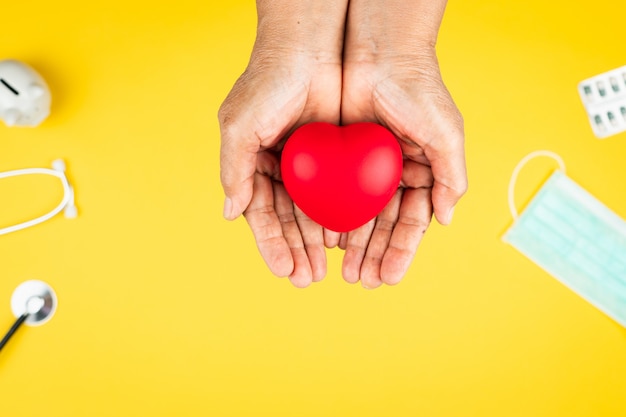 Concetto di giornata mondiale della salute assicurazione sanitaria con cuore rosso sul supporto mani della donna senior
