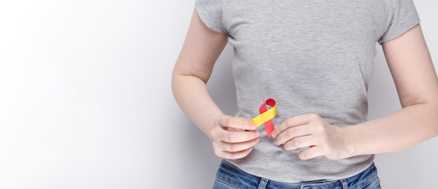 Concetto di giornata mondiale dell'epatite. ragazza in maglietta grigia che tiene il simbolo liveras rosso-giallo di area del nastro di consapevolezza. sfondo grigio. copia spazio