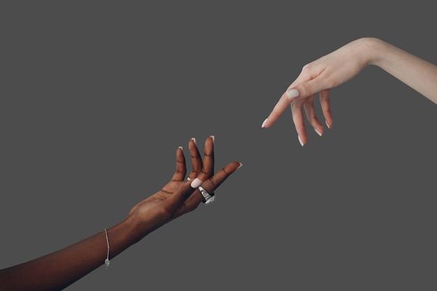 World humanitarian day. caucasian white and african american\
black hand reaching out to each other on gray background.