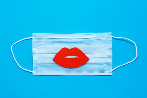 World Kiss Day. Red lips on a protective medical mask on a blue background. Coronavirus pandemic