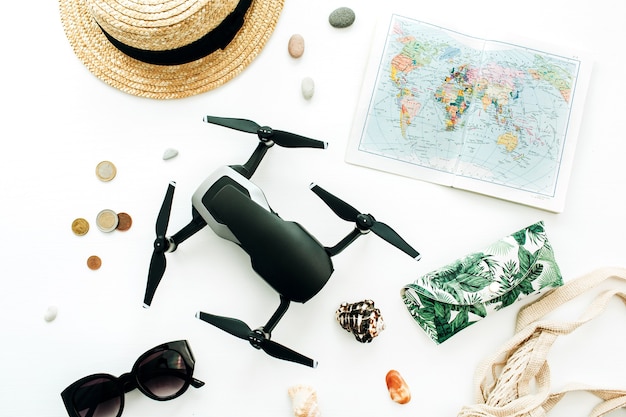 Mappa del mondo, drone, paglia, occhiali da sole, monete su sfondo bianco. disposizione piatta, vista dall'alto