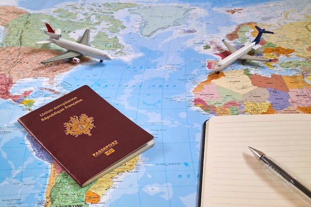 world map with on it two planes a french passport and a ballpoint pen on the top of an open note pad