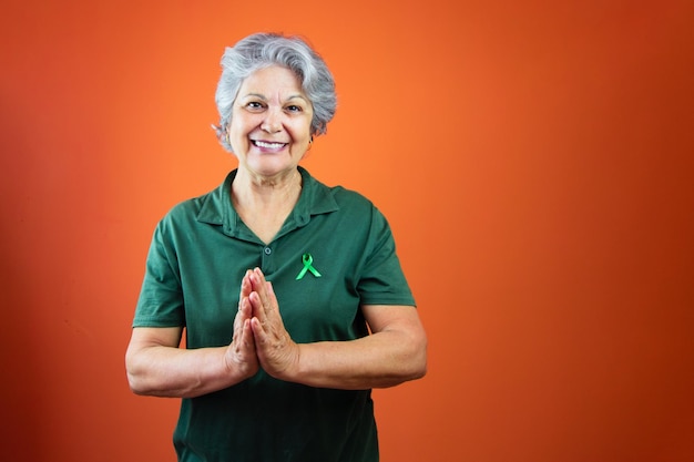 World mental health day Mature Woman With Gray Hair green ribbon and shirt isolated on orange