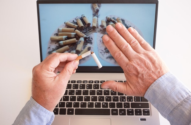 World no tobacco day caucasian male hands holding a broken\
cigarette over laptop keyboard ready to stop smoking