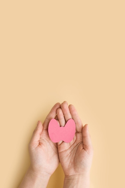 Photo world thyroid day women's hands hold a paper form of the thyroid gland on beige background