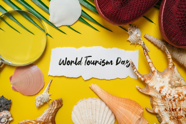 World Tourism Day incription over yellow background, with palm leaves, clam shell, and shoes flat lay background