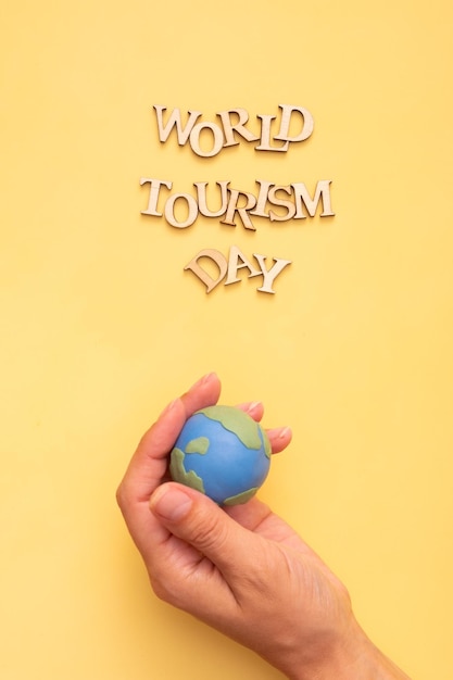 Photo world tourism day text from wooden letters on a yellow background with globe in hand