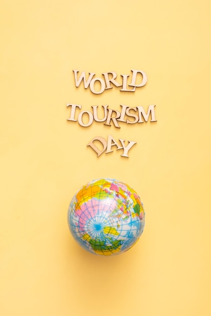 World Tourism Day text from wooden letters on a yellow background with globe Vertical format