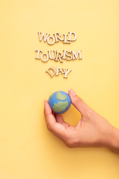 World Tourism Day text from wooden letters on a yellow color background with globe in female hands top view